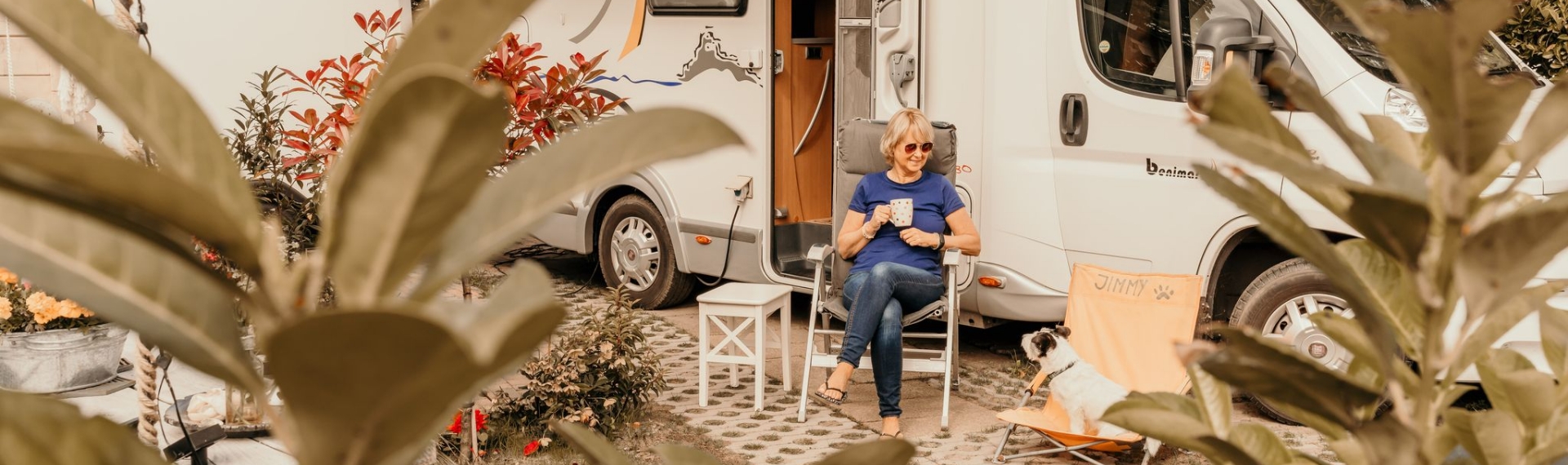 Campinggast zit ontspannen bij de camper met hond op camping Kotestee in Ouddorp.