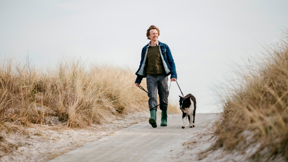 Man wandelt met hond over het duinpad bij de Westduinen in Ouddorp nabij camping Kotestee.