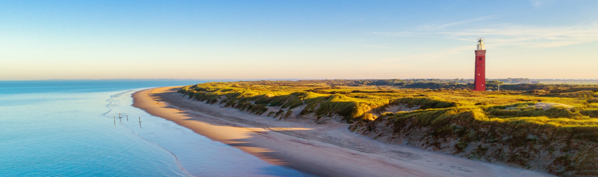 Panoramafoto van het strand en de rode vuurtoren Westhoofd bij Ouddorp.