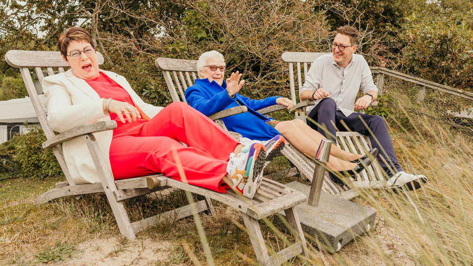 Drie generaties familie ontspannen en lachen samen op houten ligstoelen op camping Kotestee.