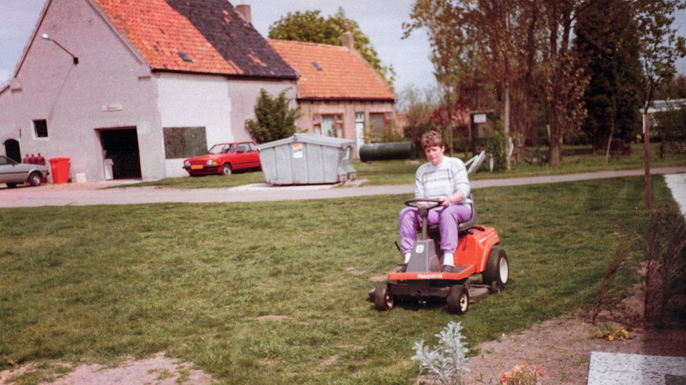 Truus Polie op een zitmaaier maait het gras op het erf van de boerderij van Kotestee in de jaren tachtig.
